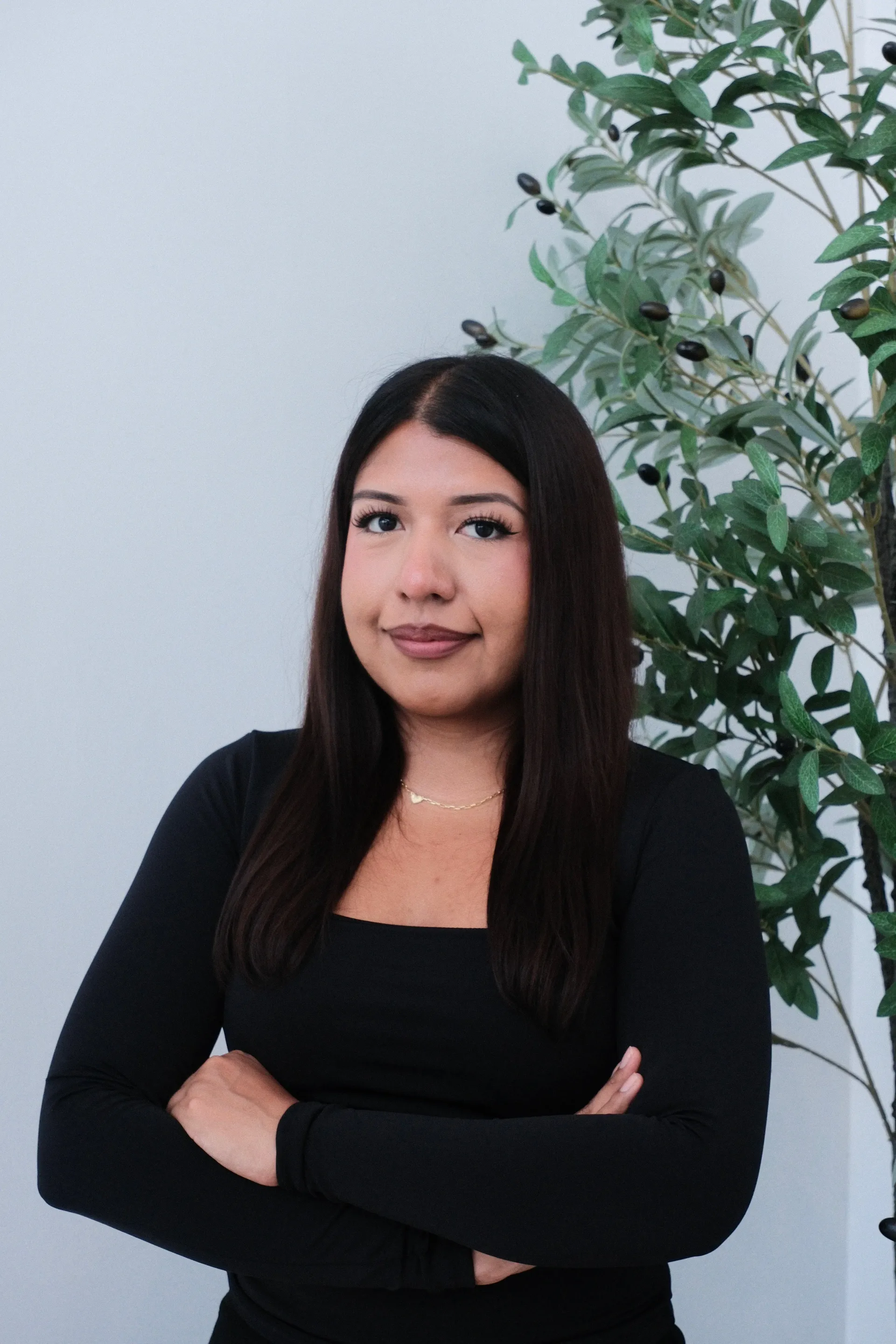 Michell Montesinos in a black top with her arms crossed, standing beside a leafy plant